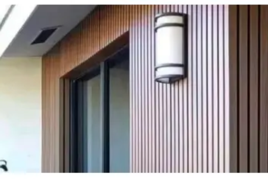 Bruno kültéri WPC falburkolat homlokzati részlet nyílászáró és kültéri fali lámpa mellett, lamellás kialakítással.